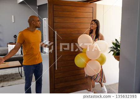 Welcoming African American woman with balloons entering home, greeted by smiling man Welcoming African American woman with balloons entering home, greeted by smiling man 135632393