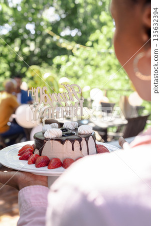Carrying birthday cake with strawberries, person at outdoor celebration with people Carrying birthday cake with strawberries, person at outdoor celebration with people 135632394