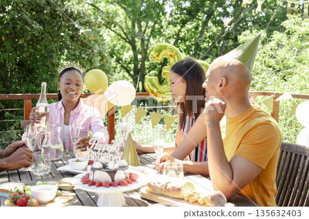 Celebrating birthday outdoors, friends enjoying cake and drinks on sunny day Celebrating birthday outdoors, friends enjoying cake and drinks on sunny day 135632403