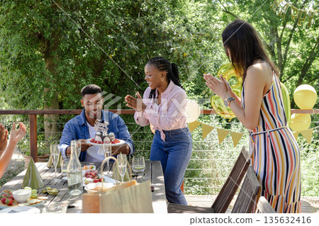 Receiving birthday cake from friends, African American man smiling joyfully outdoors Receiving birthday cake from friends, African American man smiling joyfully outdoors 135632416