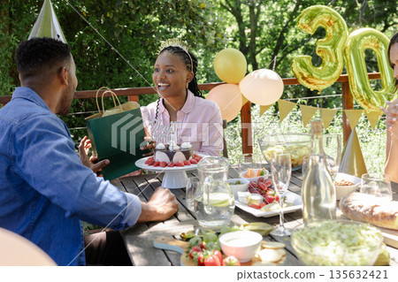 Receiving gift at outdoor party, African American woman celebrating birthday with friends 135632421