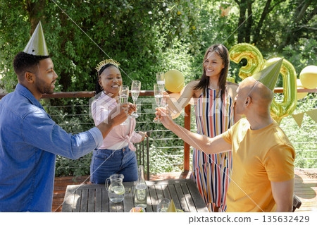 Celebrating outdoors, friends toasting with champagne and wearing party hats, smiling Celebrating outdoors, friends toasting with champagne and wearing party hats, smiling 135632429