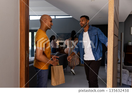 African American man welcoming guest with gift bag at home celebration African American man welcoming guest with gift bag at home celebration 135632438