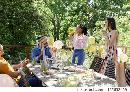 Friends celebrating birthday outdoors with balloons and decorations, enjoying moment Friends celebrating birthday outdoors with balloons and decorations, enjoying moment 135632439