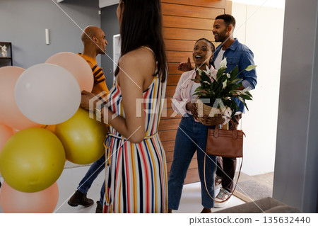 Friends arriving at home with balloons and plant, celebrating together joyfully 135632440