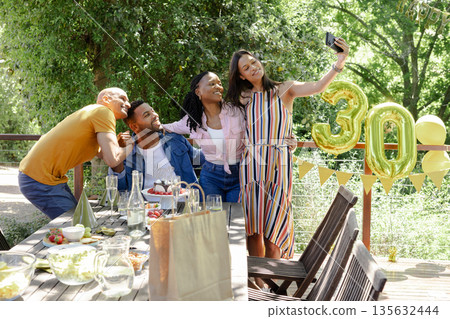 Friends celebrating 30th birthday outdoors, taking selfie with golden balloons 135632444