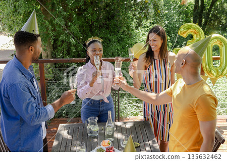 Celebrating birthday outdoors, friends toasting with champagne wearing party hats 135632462