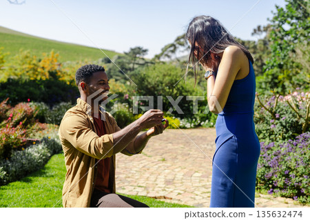 Man proposing to surprised woman in garden, capturing joyful engagement moment 135632474