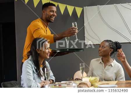 African American man serving champagne to friends at festive dinner party 135632490