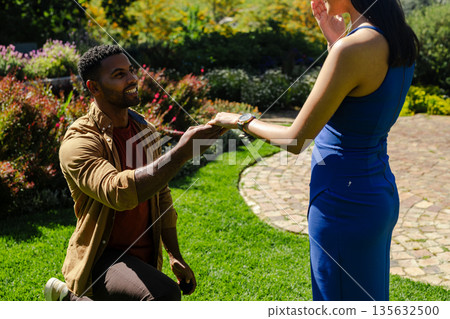 African American man proposing to woman in garden, both looking joyful and excited 135632500
