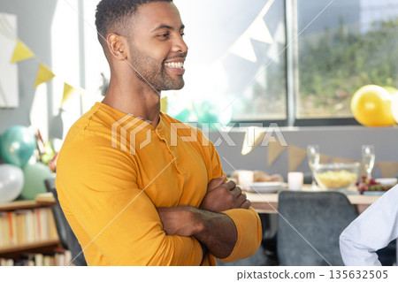 Smiling man in yellow shirt enjoying festive gathering with balloons and decorations 135632505