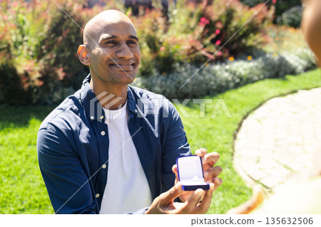 Man proposing with ring box in garden, smiling and looking hopeful 135632506