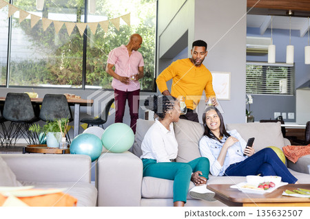 Friends enjoying casual gathering at home, chatting and laughing on couch 135632507