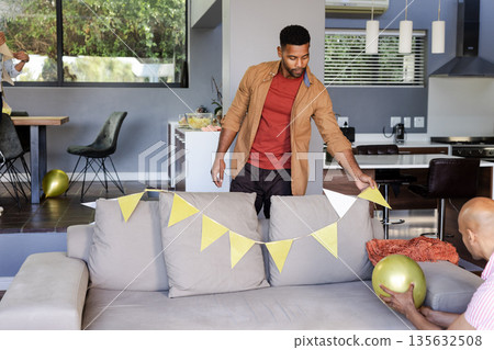 Man decorating living room with gold balloons and bunting for celebration Man decorating living room with gold balloons and bunting for celebration 135632508
