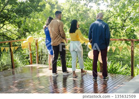 Friends enjoying outdoor celebration on wooden deck surrounded by lush greenery 135632509