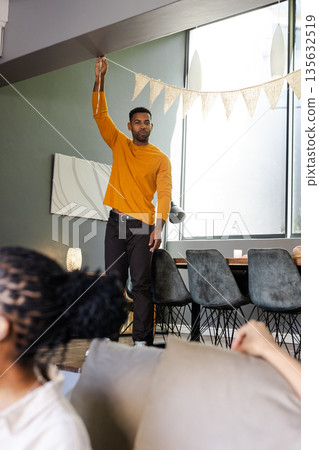 African American man decorating living room with bunting for celebration African American man decorating living room with bunting for celebration 135632519