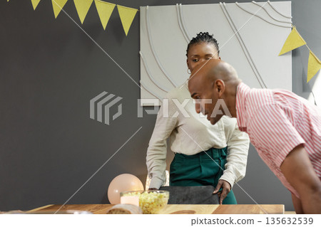 Man and woman preparing for celebration, arranging table with snacks and decorations Man and woman preparing for celebration, arranging table with snacks and decorations 135632539