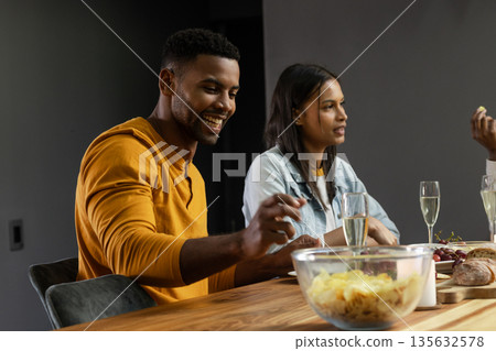 Friends enjoying snacks and drinks at home, smiling and chatting together Friends enjoying snacks and drinks at home, smiling and chatting together 135632578