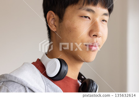Young man with headphones around neck looking thoughtfully, wearing casual hoodie Young man with headphones around neck looking thoughtfully, wearing casual hoodie 135632614
