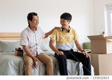 Father and son unpacking boxes in bedroom, sharing joyful moment together Father and son unpacking boxes in bedroom, sharing joyful moment together 135632621
