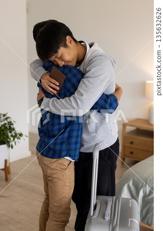 Two people hugging warmly at home, one holding passport and suitcase Two people hugging warmly at home, one holding passport and suitcase 135632626