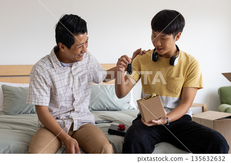 Father and son sharing joyful moment with car key gift on bed Father and son sharing joyful moment with car key gift on bed 135632632
