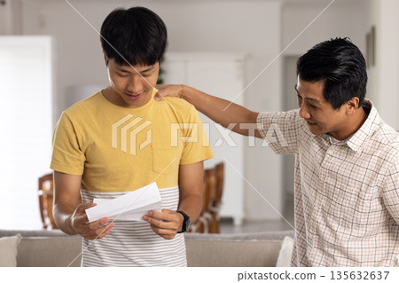 Father congratulating son reading letter at home, both smiling with joy 135632637