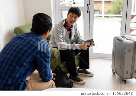 Friends discussing travel plans at home with suitcase and passport Friends discussing travel plans at home with suitcase and passport 135632648