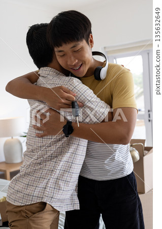 Young man hugging father, holding car keys, celebrating new car at home 135632649