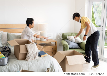 Friends unpacking boxes and organizing bedroom, creating cozy living space together Friends unpacking boxes and organizing bedroom, creating cozy living space together 135632654