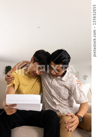 Father and son celebrating good news together while reading letter on couch Father and son celebrating good news together while reading letter on couch 135632655