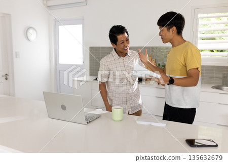 Father and son discussing documents in kitchen with laptop and coffee mug Father and son discussing documents in kitchen with laptop and coffee mug 135632679
