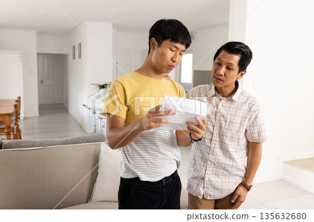 Father and son reading letter together at home, discussing important news Father and son reading letter together at home, discussing important news 135632680