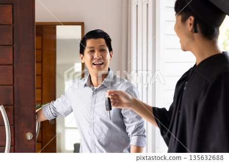 Father welcoming graduate son home, smiling as he receives car keys at door Father welcoming graduate son home, smiling as he receives car keys at door 135632688