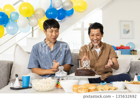 Celebrating birthday, two friends clapping and smiling with cake in living room Celebrating birthday, two friends clapping and smiling with cake in living room 135632692
