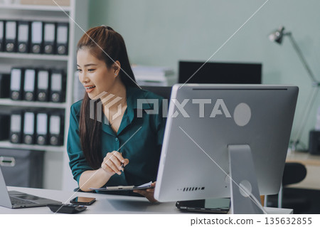 Determined asian businesswoman works late in a modern office, confidently analyzing data on her laptop, embodying success and professionalism with a smile Determined asian businesswoman works late in a modern office, confidently analyzing data on her laptop, embodying success and professionalism with a smile 135632855