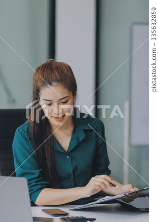 Determined asian businesswoman works late in a modern office, confidently analyzing data on her laptop, embodying success and professionalism with a smile Determined asian businesswoman works late in a modern office, confidently analyzing data on her laptop, embodying success and professionalism with a smile 135632859