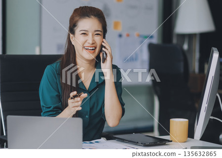 Determined asian businesswoman works late in a modern office, confidently analyzing data on her laptop, embodying success and professionalism with a smile Determined asian businesswoman works late in a modern office, confidently analyzing data on her laptop, embodying success and professionalism with a smile 135632865
