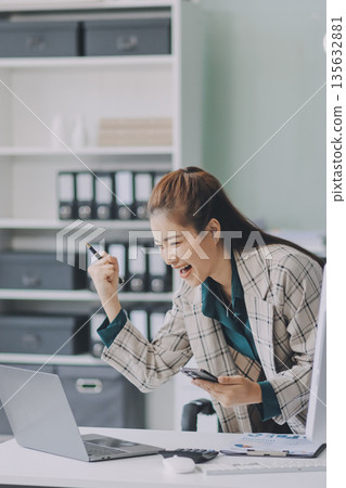 Determined asian businesswoman works late in a modern office, confidently analyzing data on her laptop, embodying success and professionalism with a smile Determined asian businesswoman works late in a modern office, confidently analyzing data on her laptop, embodying success and professionalism with a smile 135632881