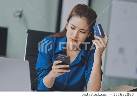 Young businesswoman is holding two credit cards with a worried expression, trying to decide which one to use to pay off her debt 135632896