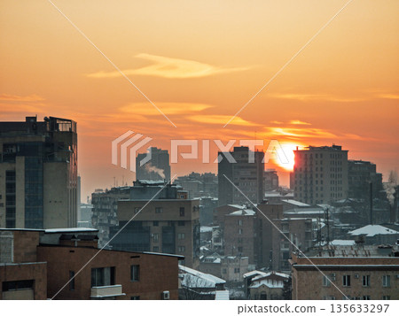 Yerevan Armenia 1.10.2026. The sun is setting over a city with tall buildings and a few clouds in the sky 135633297