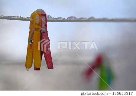 A red and yellow clothespin is hanging on a line A red and yellow clothespin is hanging on a line 135633517
