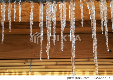 Icicles hanging from a roof, they are clear and shiny 135633523