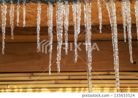 Icicles hanging from a roof, they are clear and shiny 135633524