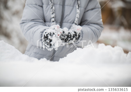 A person wearing a grey coat and gloves is playing in the snow 135633615