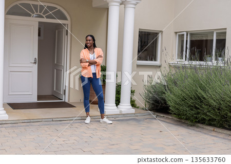 African American woman in 30s standing on stone pavers near potted plant, white door with columns African American woman in 30s standing on stone pavers near potted plant, white door with columns 135633760