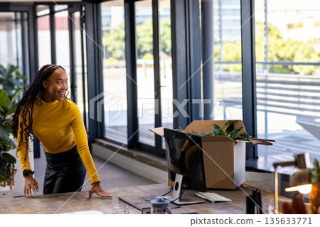 African American woman in mustard top leaning at desk looking through window in office, copy space African American woman in mustard top leaning at desk looking through window in office, copy space 135633771
