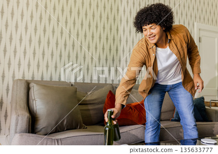 Man leaning forward beside glass coffee table picking green bottle in living room, copy space 135633777