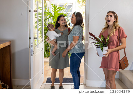 Welcoming friends at home, woman holding baby, another surprised with plant gift Welcoming friends at home, woman holding baby, another surprised with plant gift 135634379