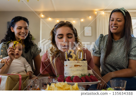 Blowing out candles, woman celebrating birthday with friends and baby at home 135634388